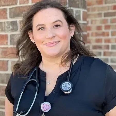 Smiling woman with stethoscope, standing outside.