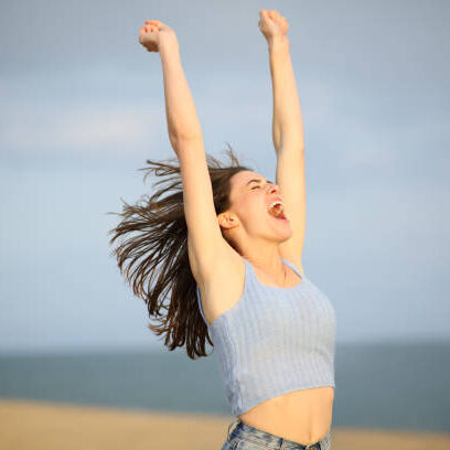 Excited woman celebrating raising arms on the beach